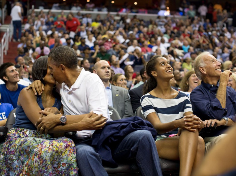 President Barack Obama kisses First Lady Michelle Obama for the "Kiss Cam" while attending the U.S. Men's Olympic basketball team's game against Brazil at the Verizon Center in Washington, D.C., July 16, 2012. Vice President Joe Biden and Malia Obama look up at the jumbotron. (Official White House Photo by Pete Souza) This official White House photograph is being made available only for publication by news organizations and/or for personal use printing by the subject(s) of the photograph. The photograph may not be manipulated in any way and may not be used in commercial or political materials, advertisements, emails, products, promotions that in any way suggests approval or endorsement of the President, the First Family, or the White House.Ê